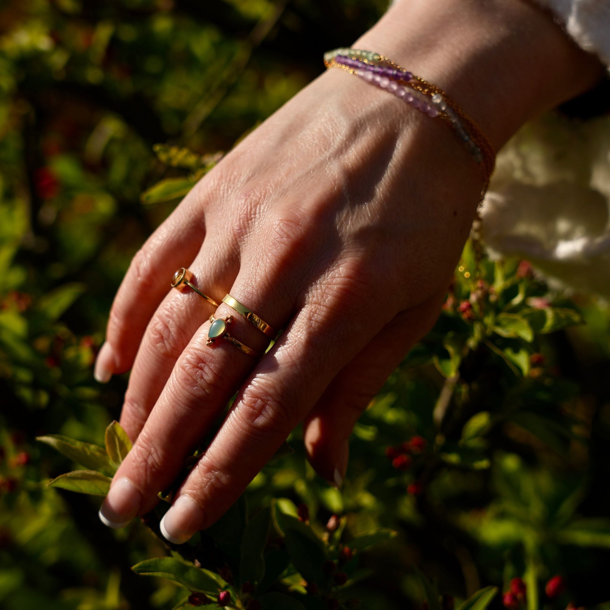 Foto van hand met diverse goldplated ringen met edelstenen op een natuurlijke achtergrond