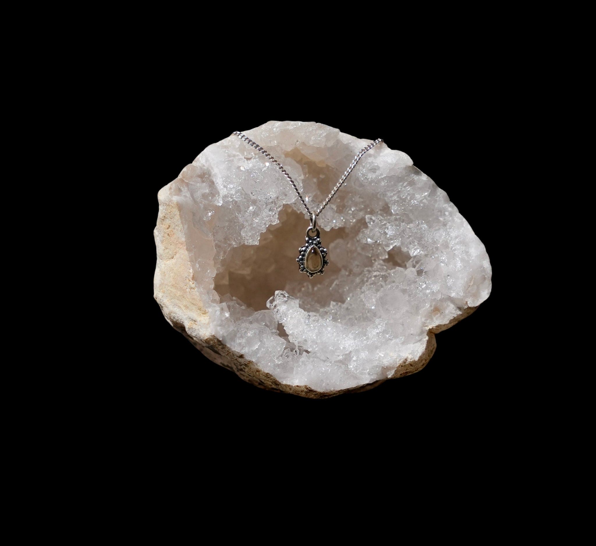 Zilveren hanger met citrien in druppelvorm met sierlijke zilveren parelrand gefotografeerd in een quarts geode