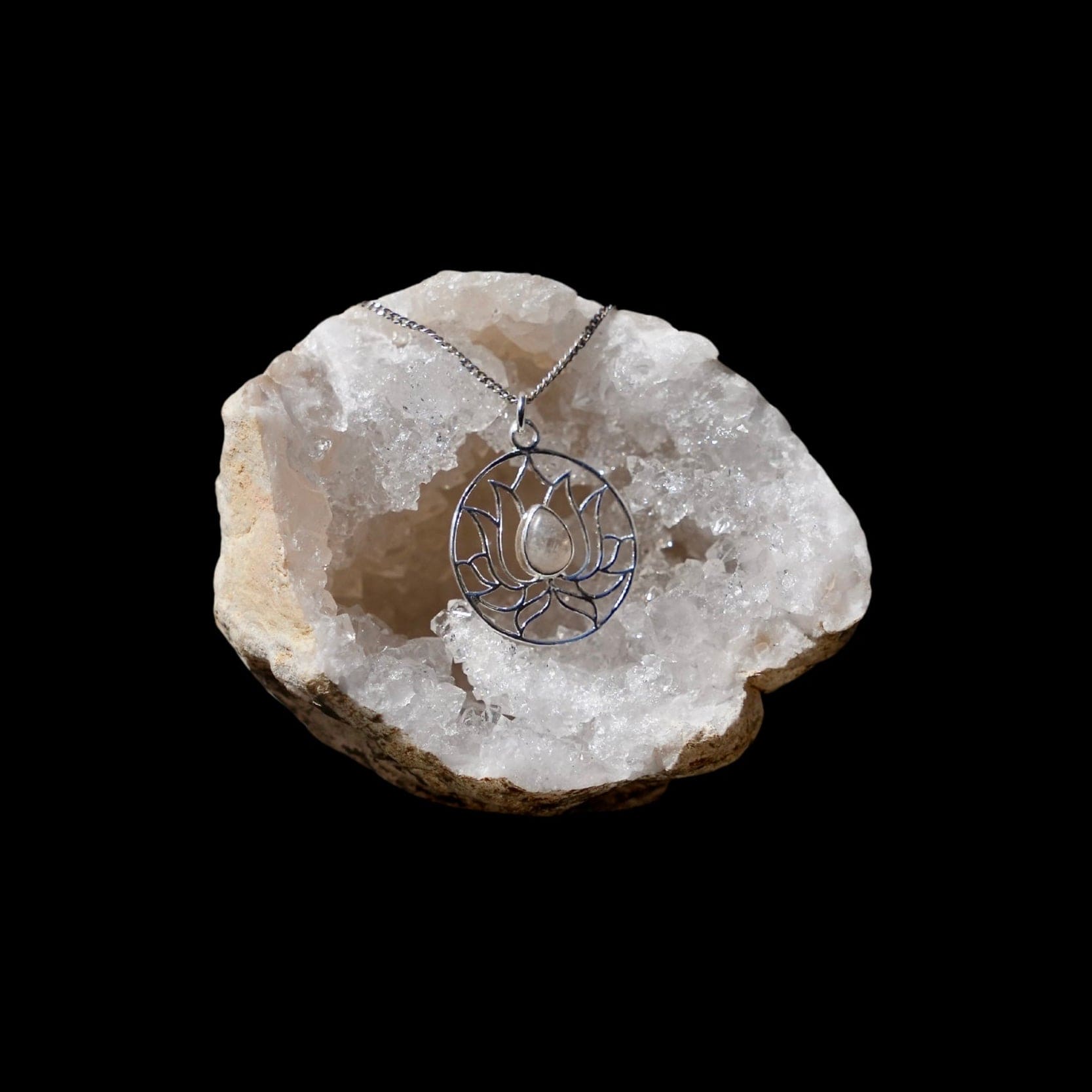 Zilveren hanger in de vorm van een omcirkelde lotusbloem met een maansteen in het midden gefotografeerd in een bergkristal geode