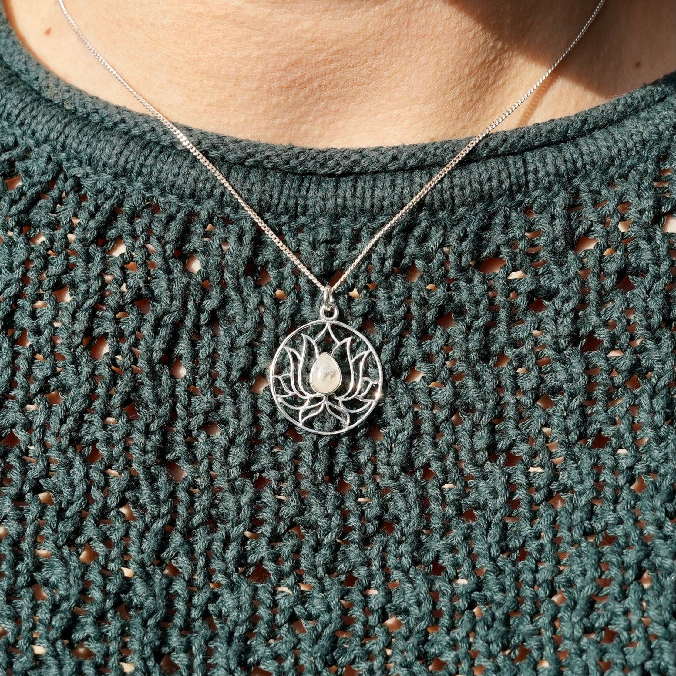 persoon met een zilveren hanger in de vorm van een omcirkelde lotusbloem met een maansteen in het midden