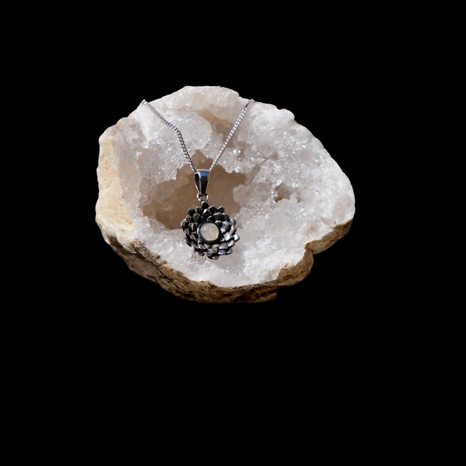 Zlveren hanger van een bovenaanzicht van een lotusbloem met een maansteen in het midden, gefotografeerd in een quarts geode
