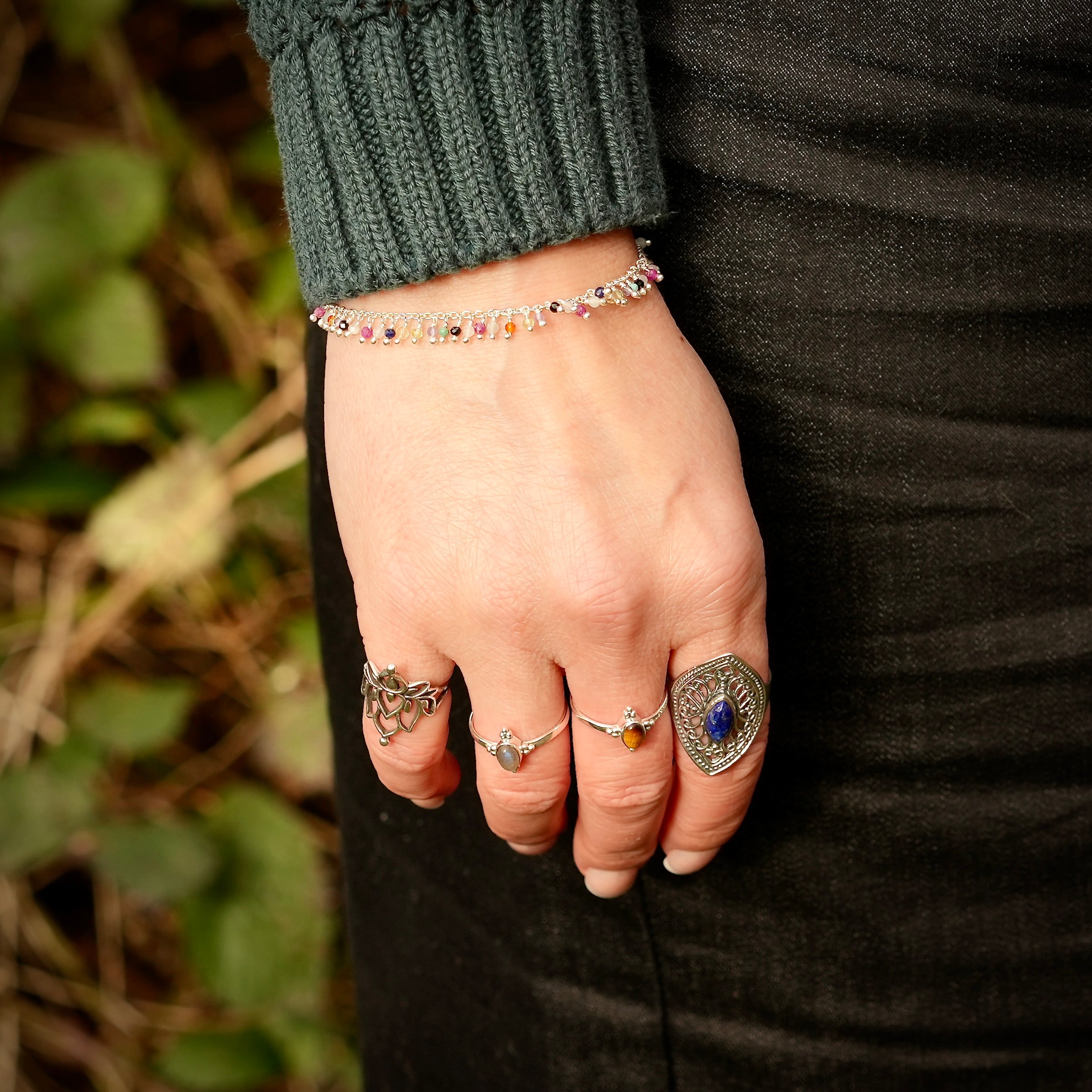 Hand met edelstenen armband en 4 ringen met edelstenen, waaronder een met Lapis Lazuli, een met tijgeroog, een met labradoriet en een ring zonder edelsteen in de vorm van een lotusbloem