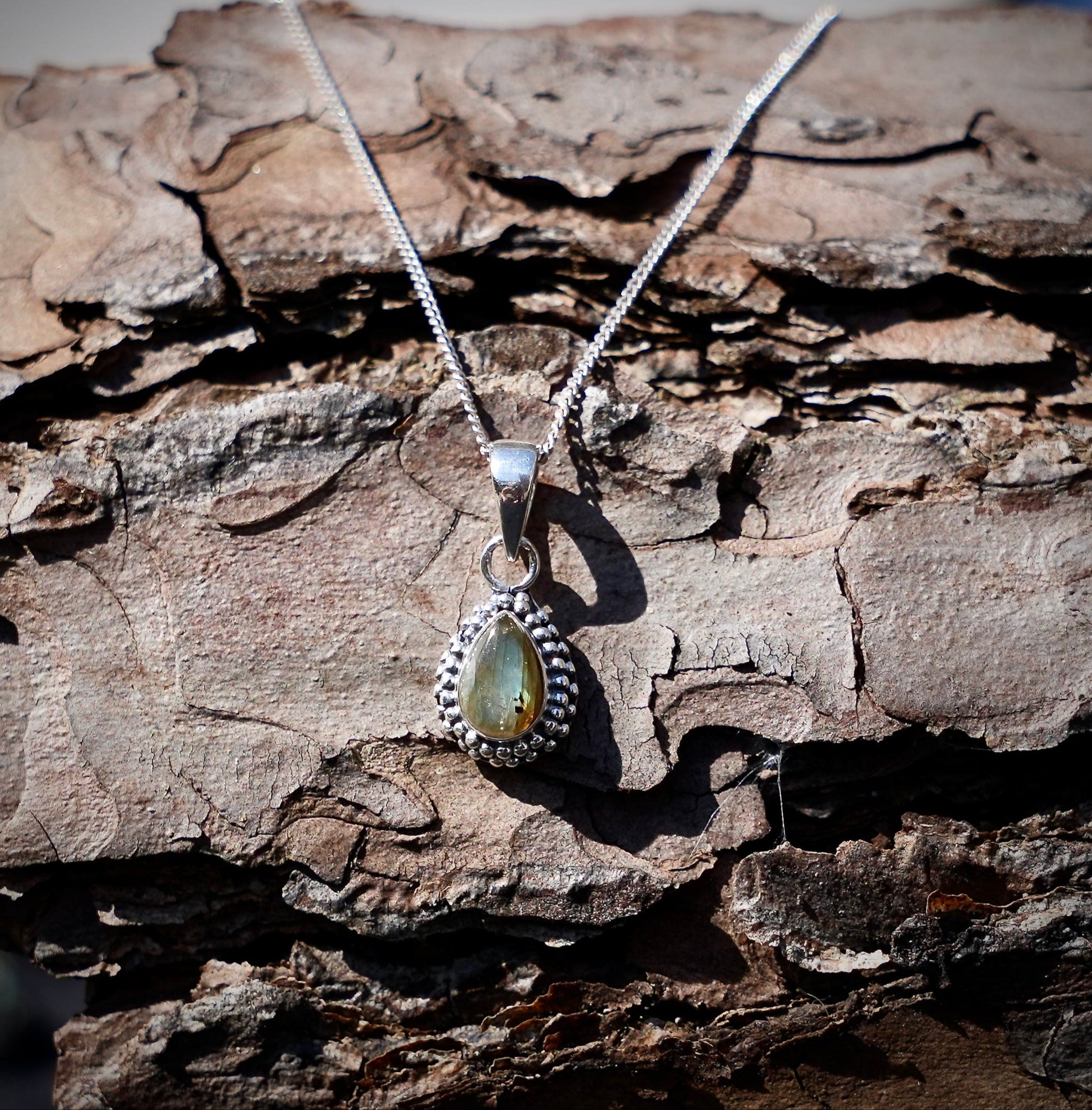 Zilveren hanger met labradoriet in druppelvorm met parelrand gefotografeerd op een achtergrond van dennenschors