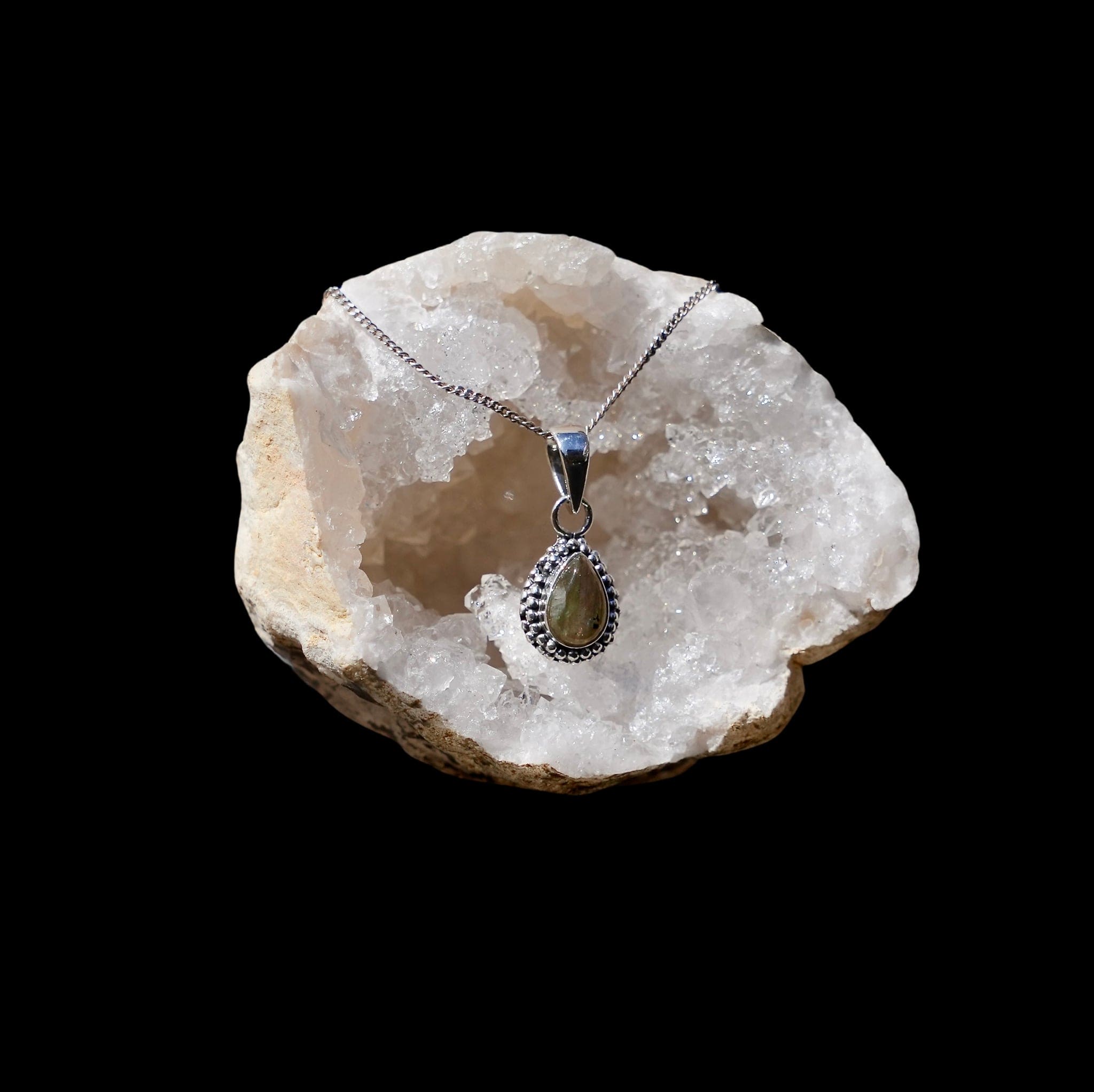Zilveren hanger met labradoriet in druppelvorm met parelrand gefotografeerd in een bergkristal geode