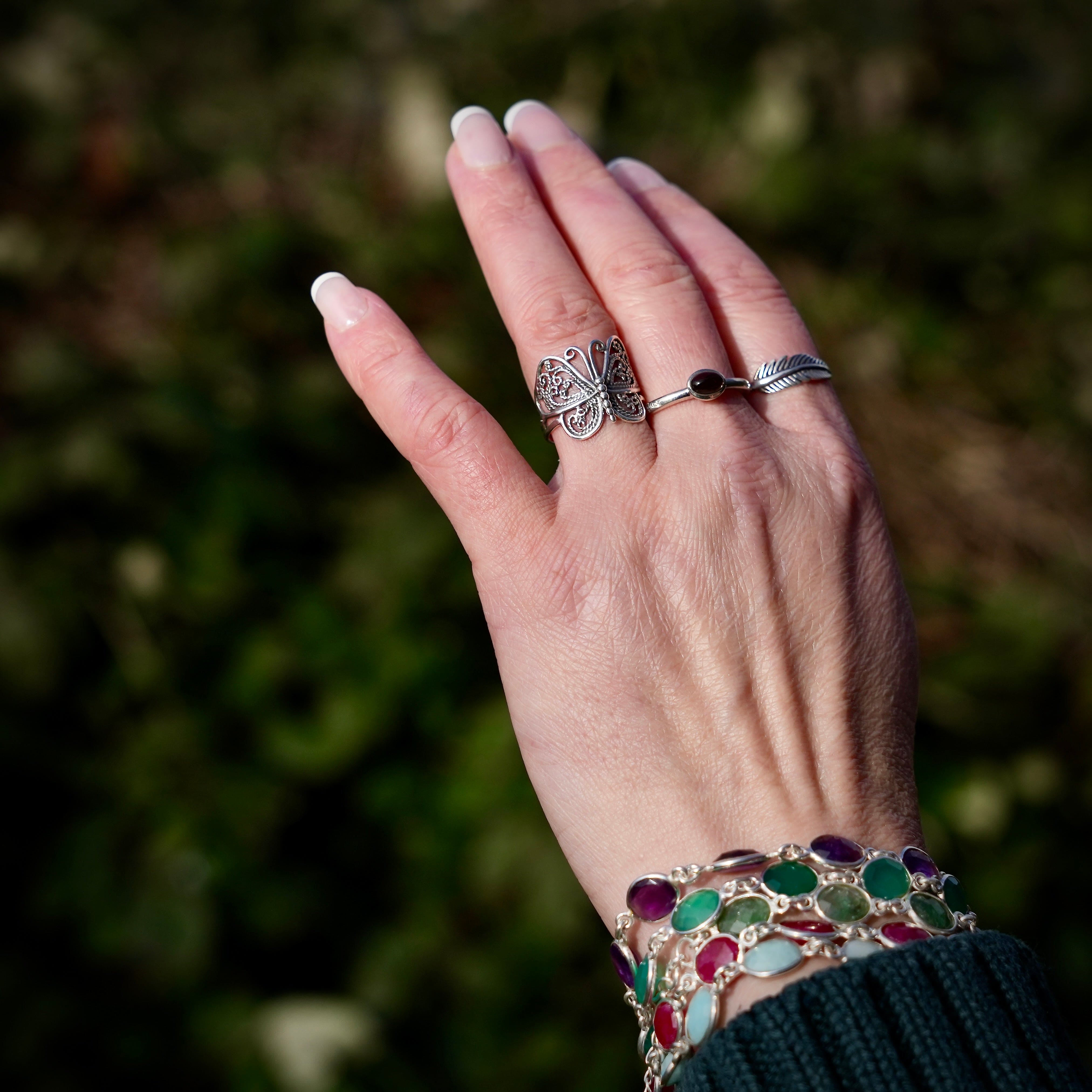 Hand met drie verschillende ringen, waaronder een in de vorm van een vlinder, een met een rookkwarts en een in de vorm van een veer en verschillende armbanden met edelstenen om de pols