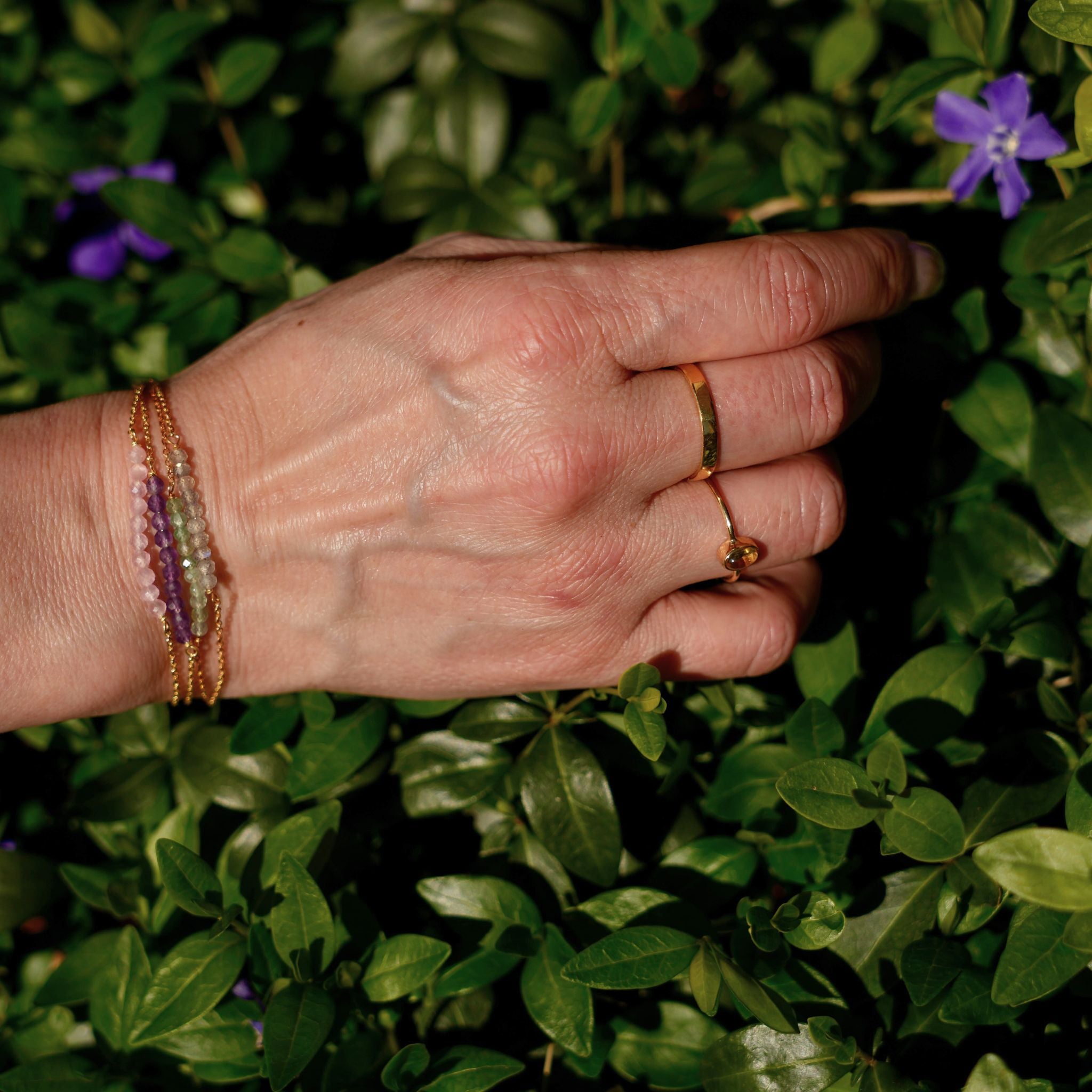 hand met verschillende goldplated ringen en armbanden met natuurlijke edelstenen